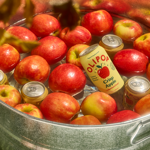 Red and yellow apples with canned beverages in a metal basin of water.