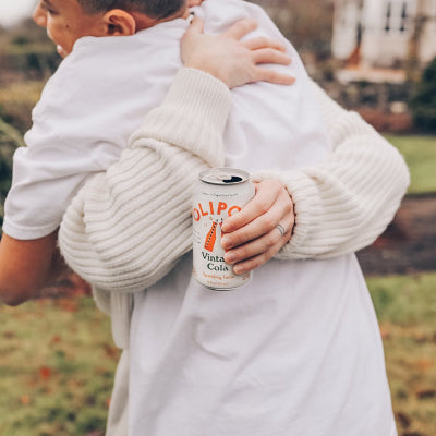 Hug between two people, with a can of olipop vintage cola.