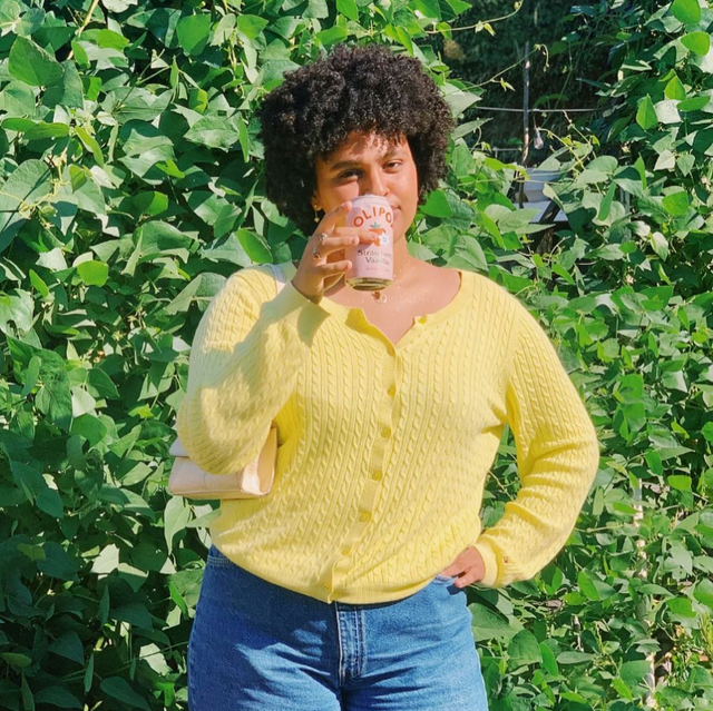 Woman wearing a yellow shirt holding a can of strawberry vanilla OLIPOP